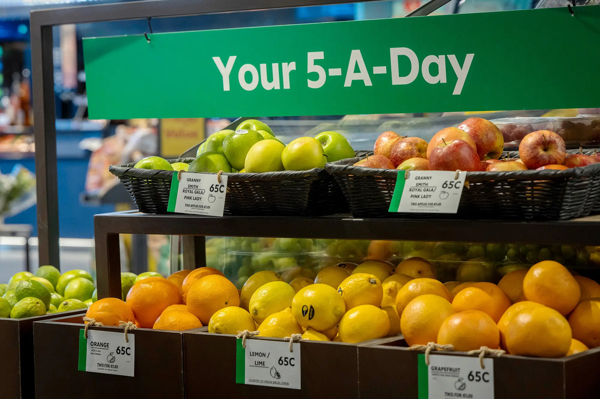 Loose produce sitting in baskets: apples, oranges, lemons and grapefruits. A banner reads Your-5-A-Day