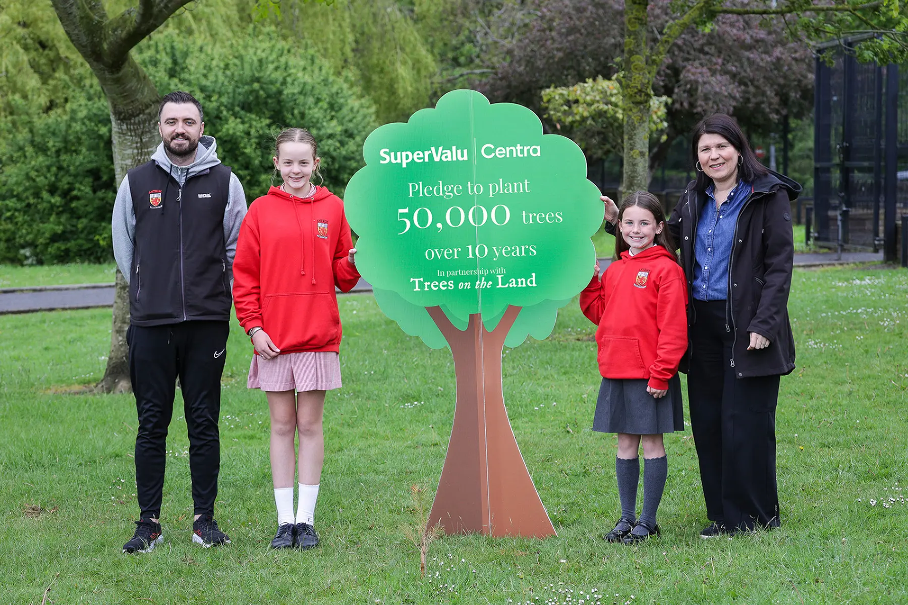 Four people stand beside a tree-shaped sign announcing SuperValu and Centra’s pledge to plant 50,000 trees over 10 years with Trees on the Land.